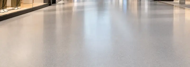 Smooth grey sheet vinyl floor in a shopping centre walkway beside shop windows